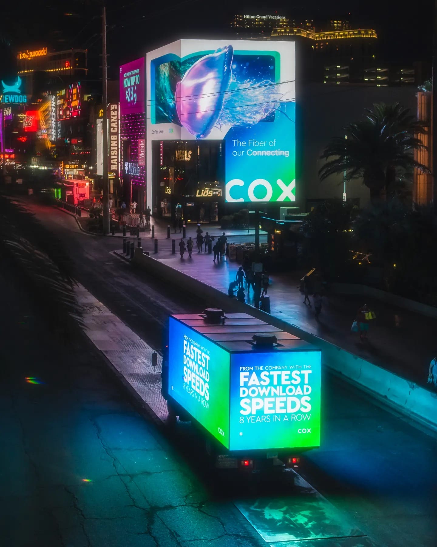 Illuminated billboards and truck ad at nighttime in city.