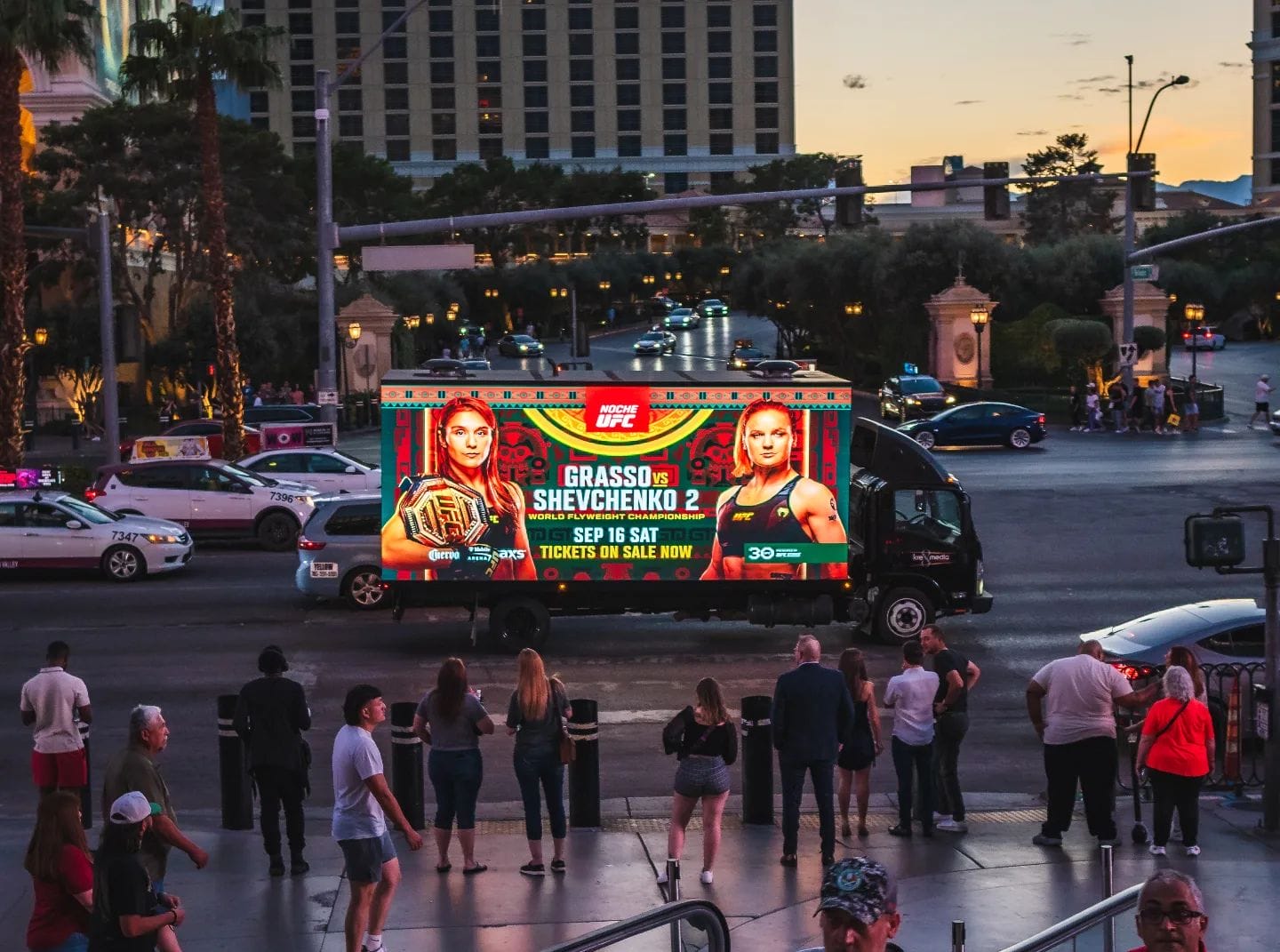 Advertising truck displaying fight event in city at dusk.