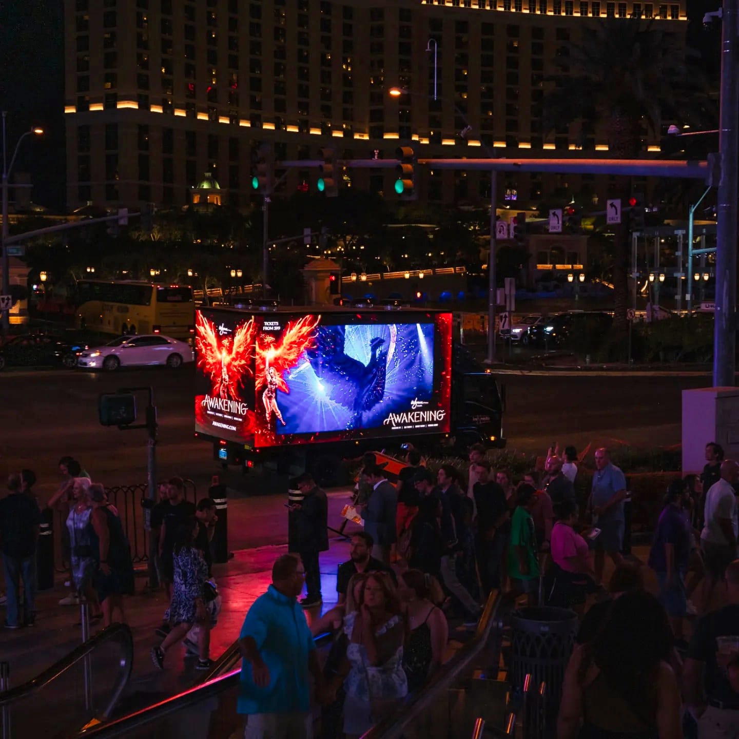 Crowd near mobile billboard with bright graphics at night.