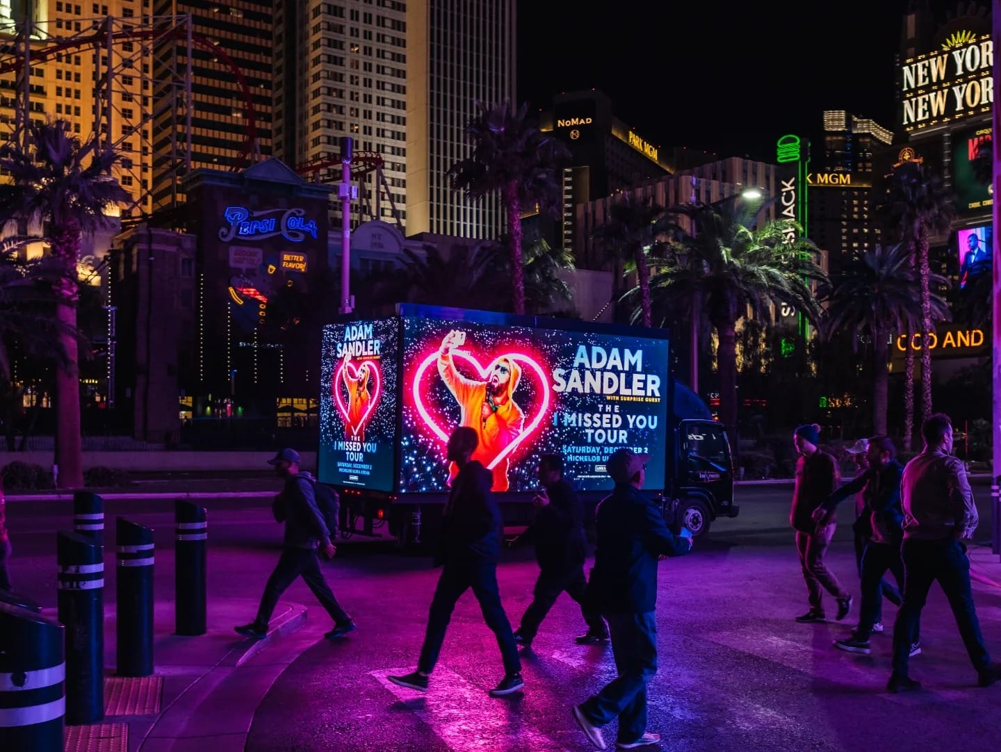 Pedestrians near Las Vegas Adam Sandler tour advertisement.