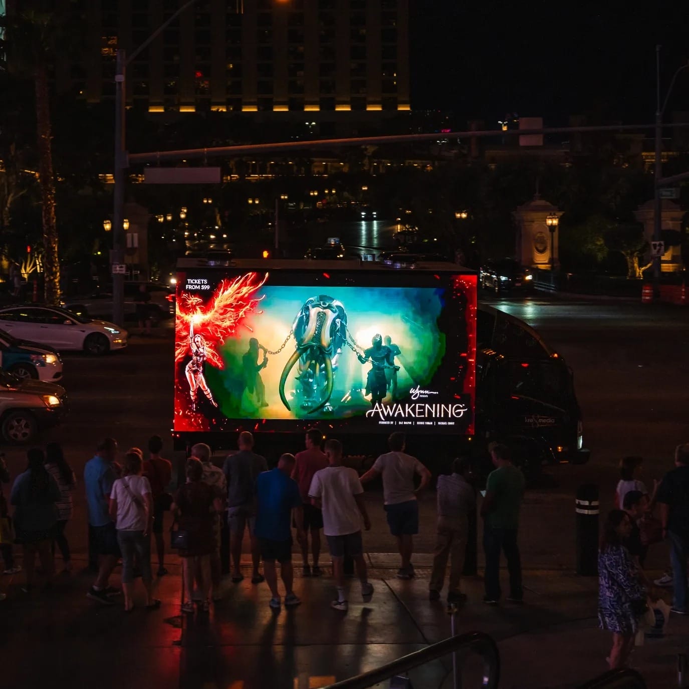 People viewing outdoor "Awakening" show advertisement at night.