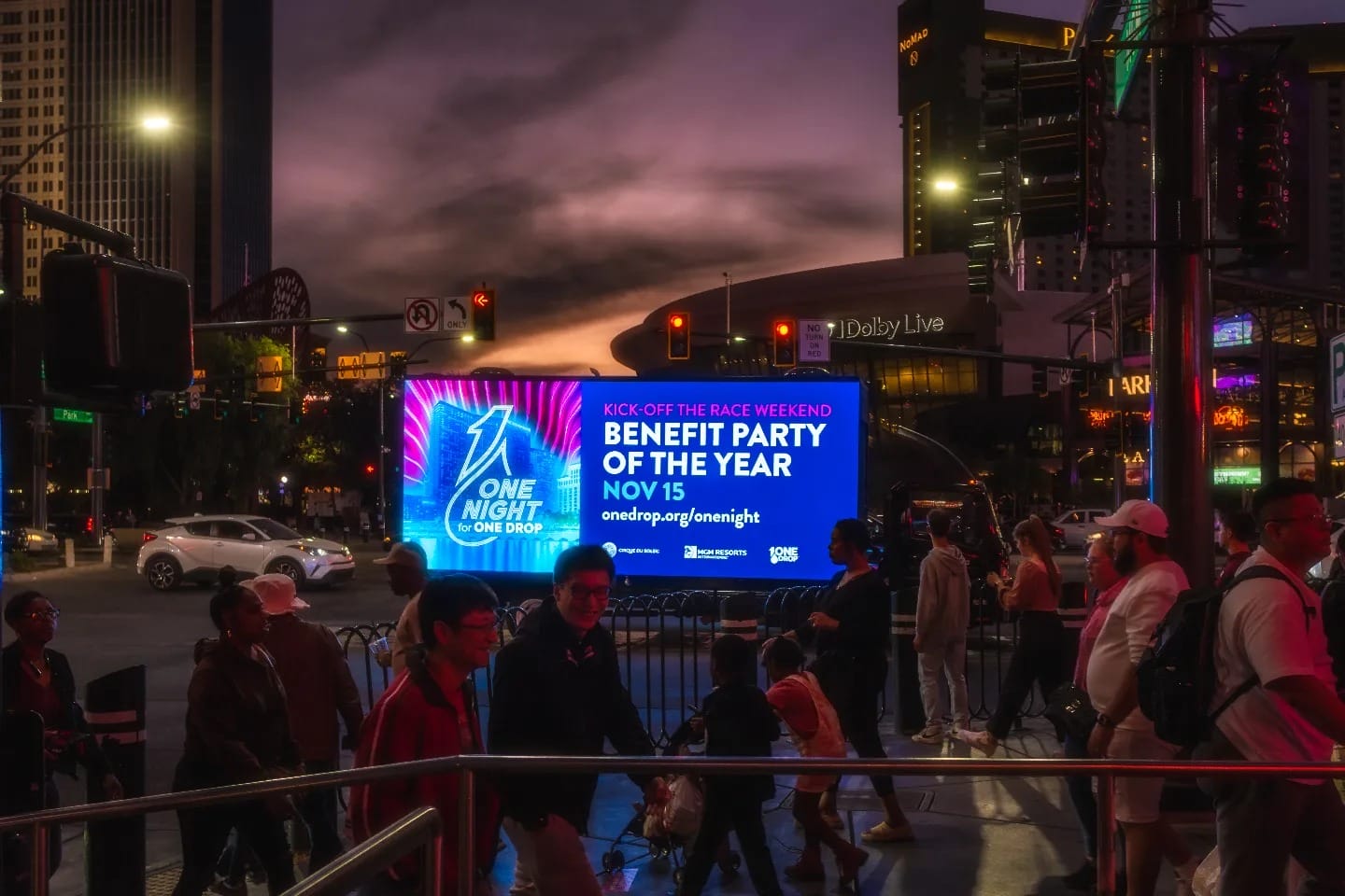 Crowd at dusk near illuminated event billboard.