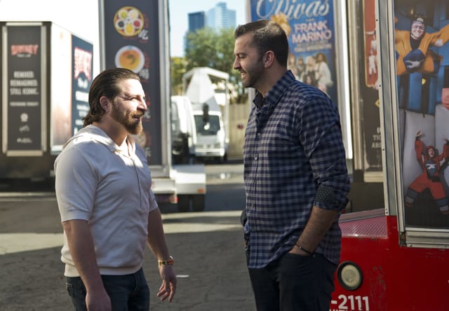 Two men talking beside food truck in sunny city