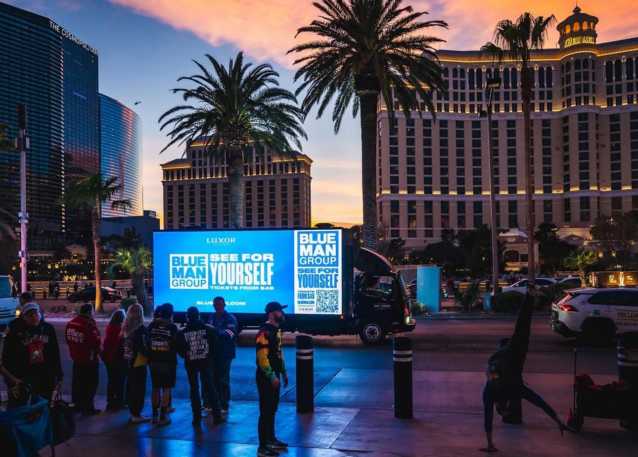 Las Vegas street scene at dusk with illuminated advertisements. Blue Man Group